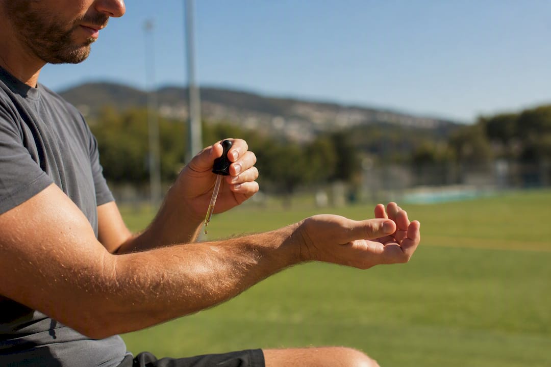 Een sporter smeert tijdens een training in de buitenlucht CBD-olie op zijn onderarm.